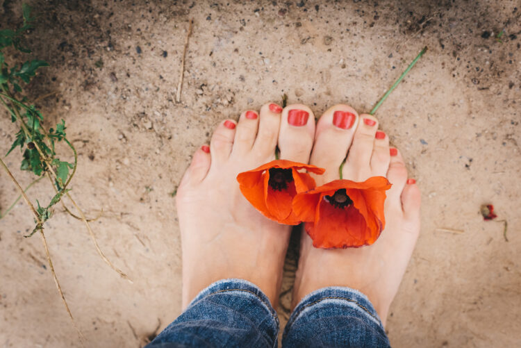 Bare feet standing on soil with two red poppies — symbolizing grounded presence and self-belonging.